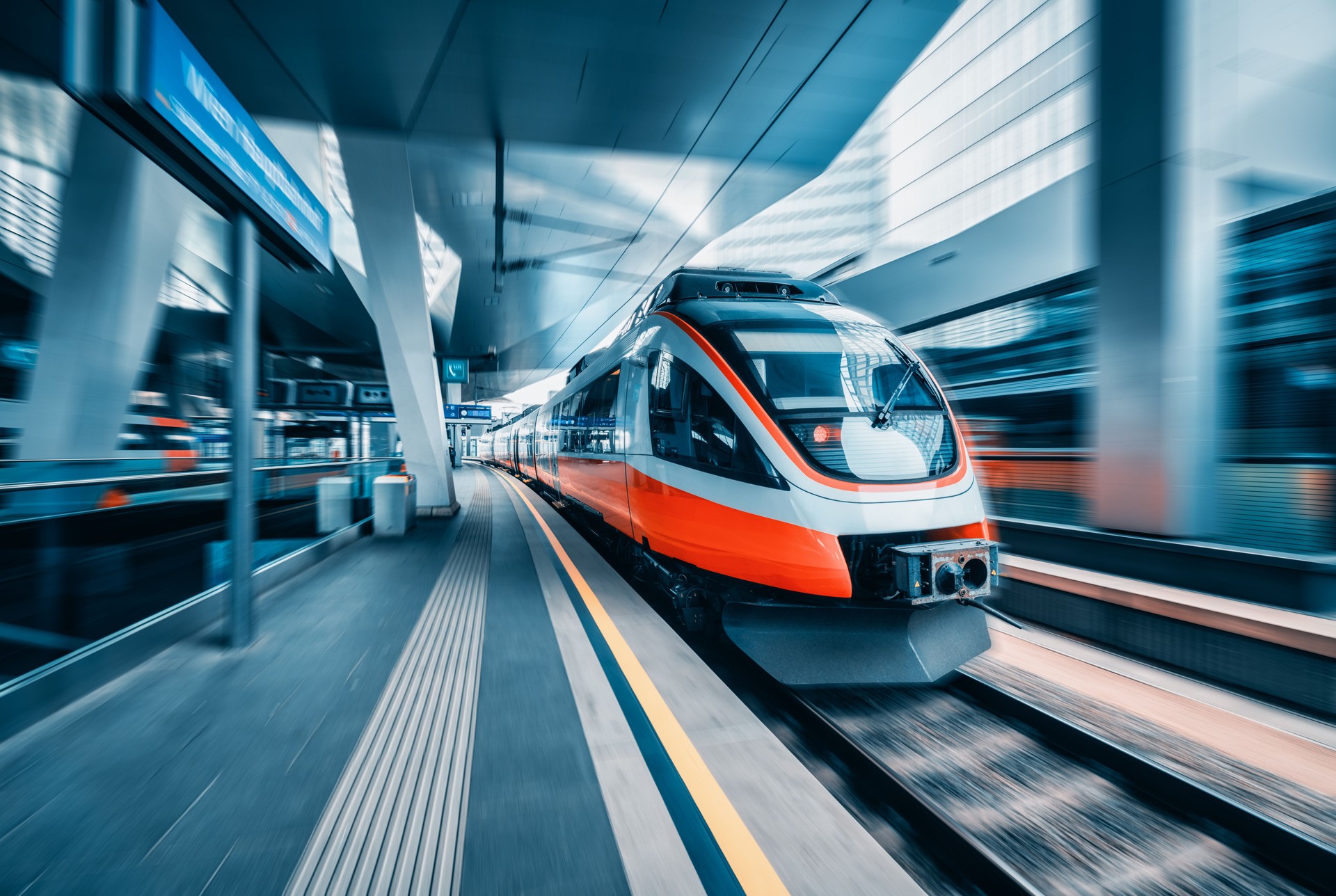 Un train à grande vitesse orange en mouvement dans une gare moderne de Vienne. Train de voyageurs interurbain rapide avec effet de flou de mouvement. Quai de gare. Chemin de fer en Autriche. Transport commercial. Concept